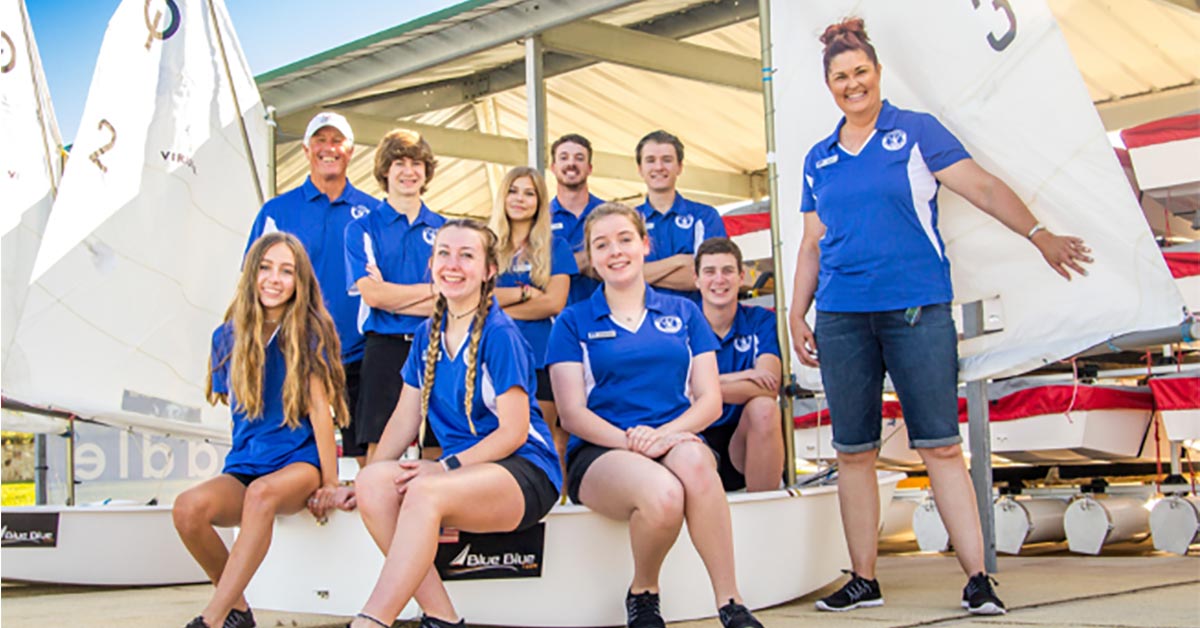 Viridian Voyagers Youth Sailing Team smiles with sailboats for a group photo.